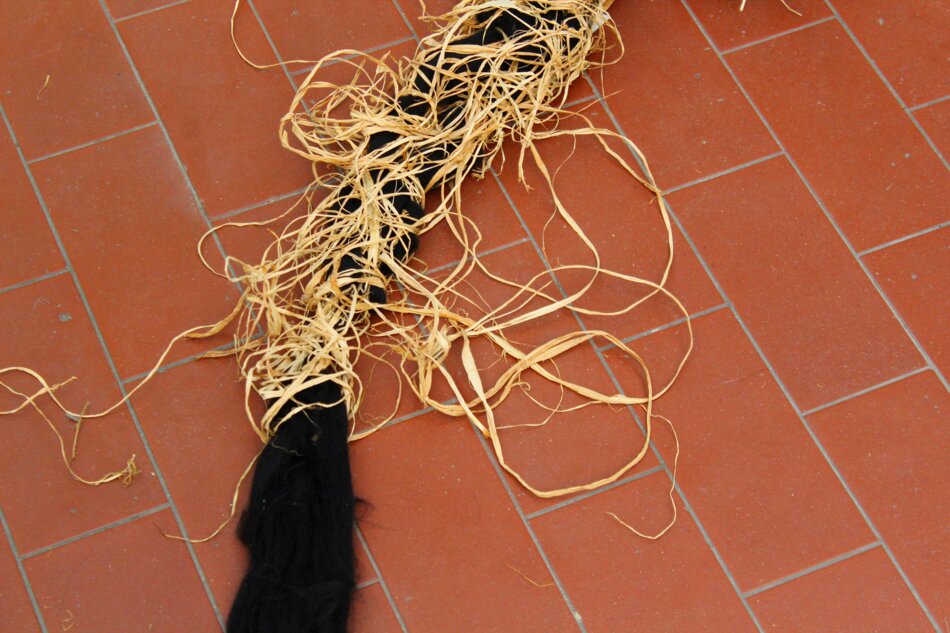 A close-up of a thick black cord wrapped with raffia, lying on a red tiled floor.