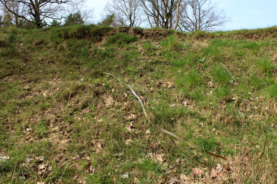 A metal strip laid across an eroded slope covered in grass and vegetation.