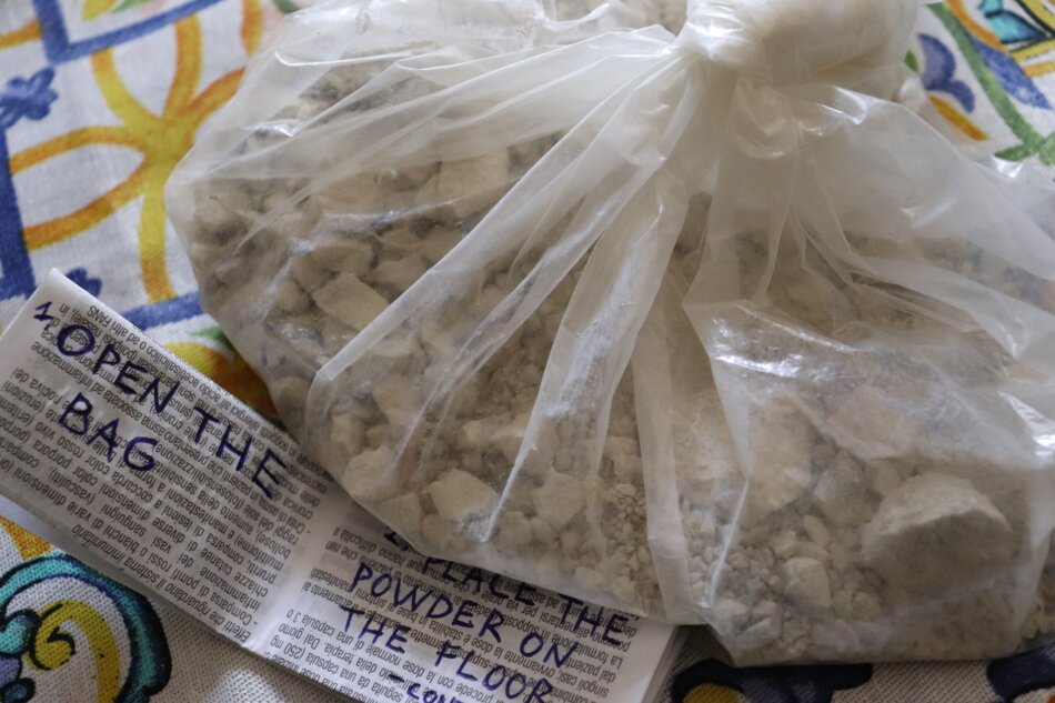 A white powder is contained in a plastic bag with a label that says “Open the Bag.” There is also a second label that says “Place the Powder on the Floor.”