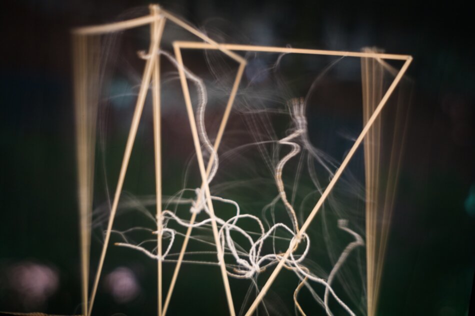 Close-up view inside a human-scale camera obscura showing a blurred, moving object made of four linden wood strip triangles, seaweed threads, and polypropylene fibers projected on the viewing surface.