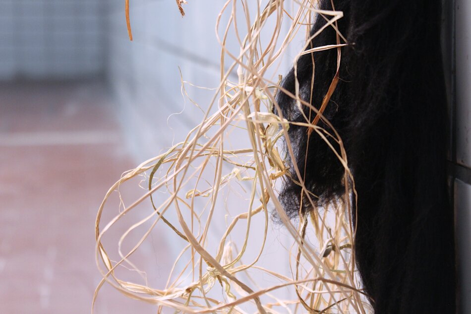 A close-up of a bundle of brown raffia and black yarn hanging from a wall.