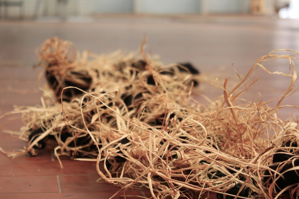 A close-up of raffia and black yarn scattered on a red tiled floor.