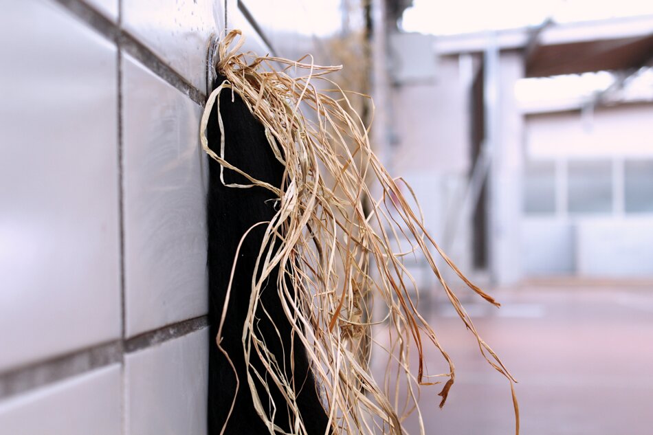 A bundle of brown raffia hanging from a black object mounted on a white tiled wall.