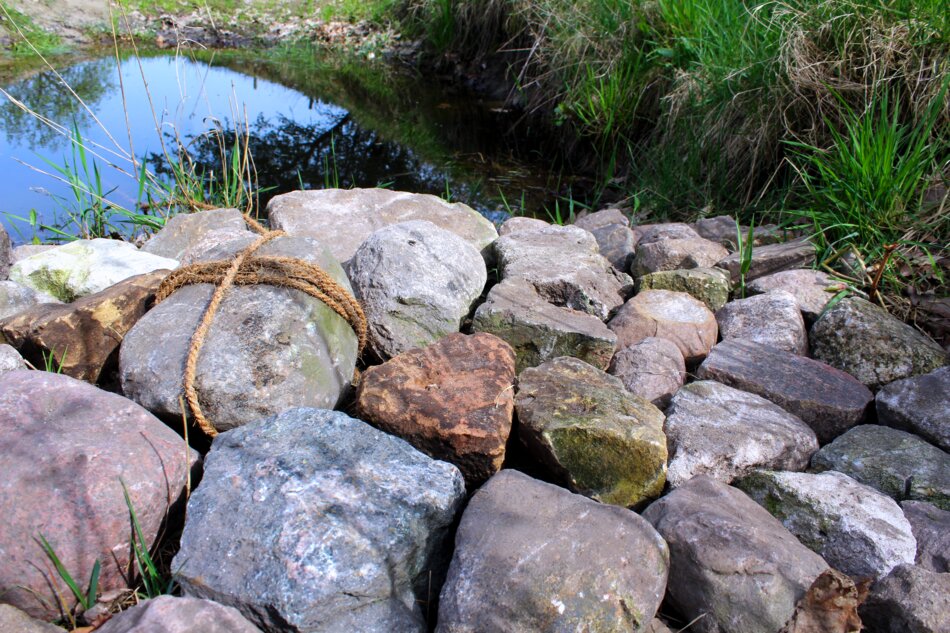 A rock dam with rope, surrounded by water and vegetation.