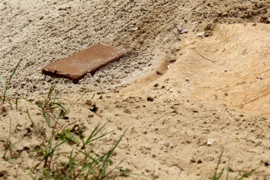 Contemporary art installation featuring sand, a brick, and an imprint resembling fabric.