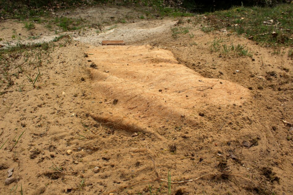 Contemporary art installation featuring soil covered with coconut fabric and a humus pillow.