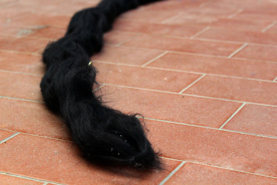 A long, thick strand of black yarn lying on a red tiled floor.