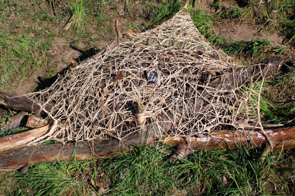 A large, intricate web made of natural fibers stretched between fallen branches in an open, rural field.