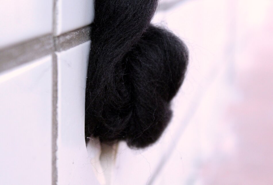 A close-up of a black, knotted mass of yarn against a white tiled wall.